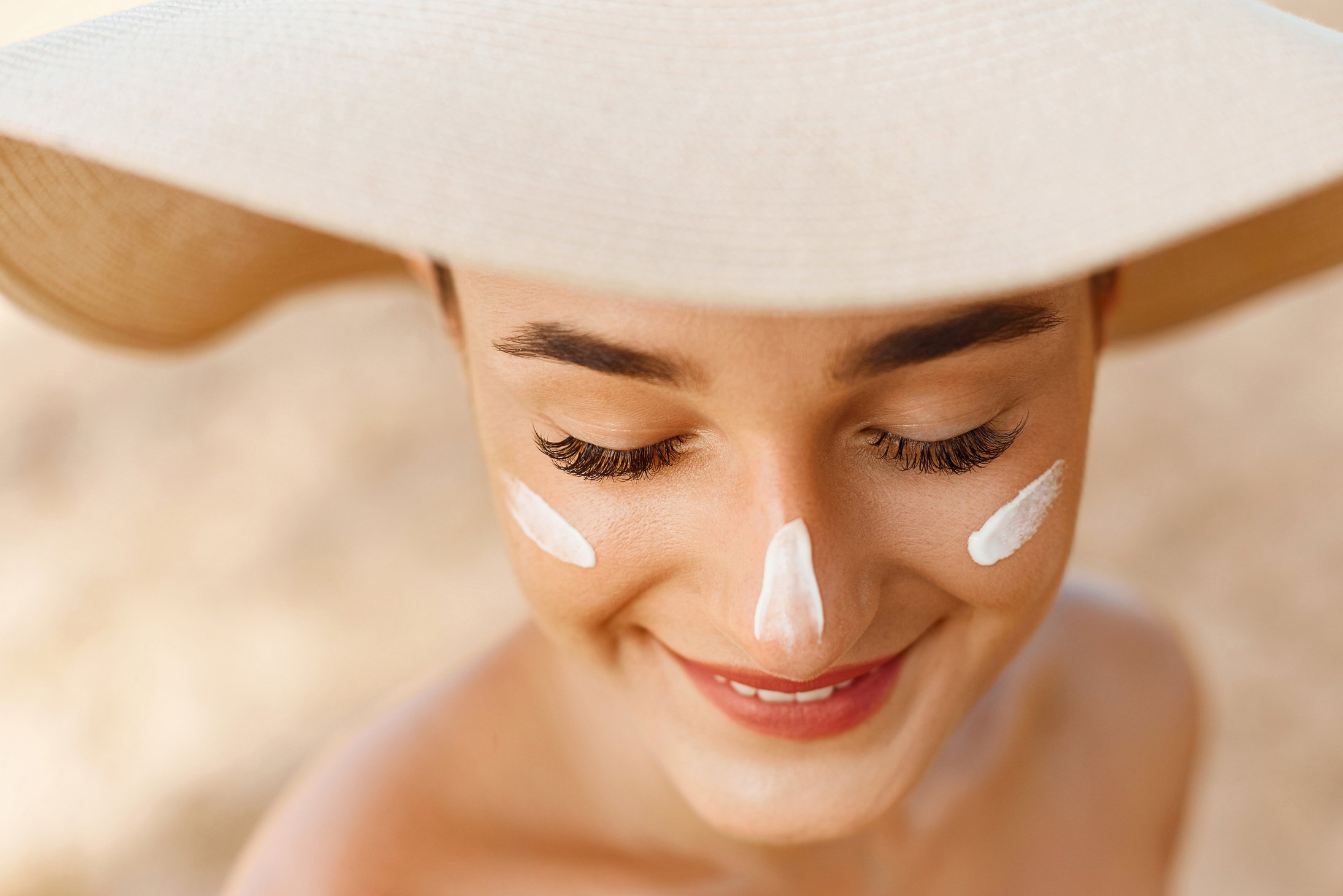 Woman smile applying sun cream  on face. Skin care. Body Sun protection. Sunscreen. Female in hat smear  moisturizing lotion on skin.Skin Protection and dermatology