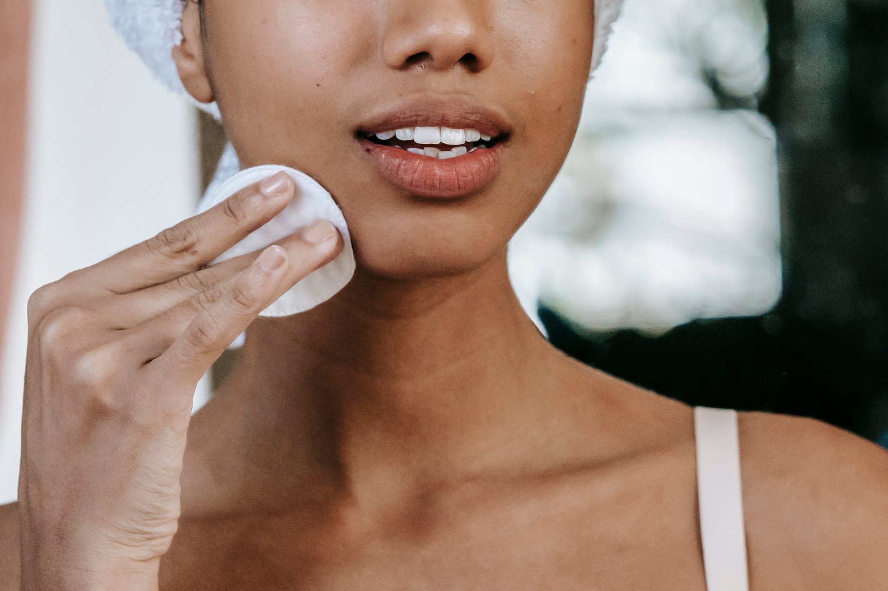 Crop ethnic woman cleaning face with cotton pad