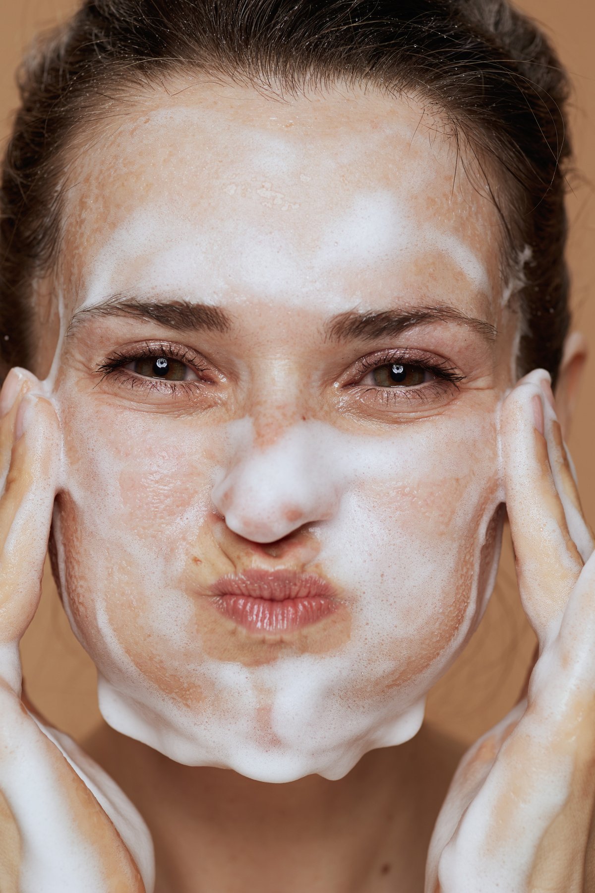 smiling young female with foaming facial cleanser washing face