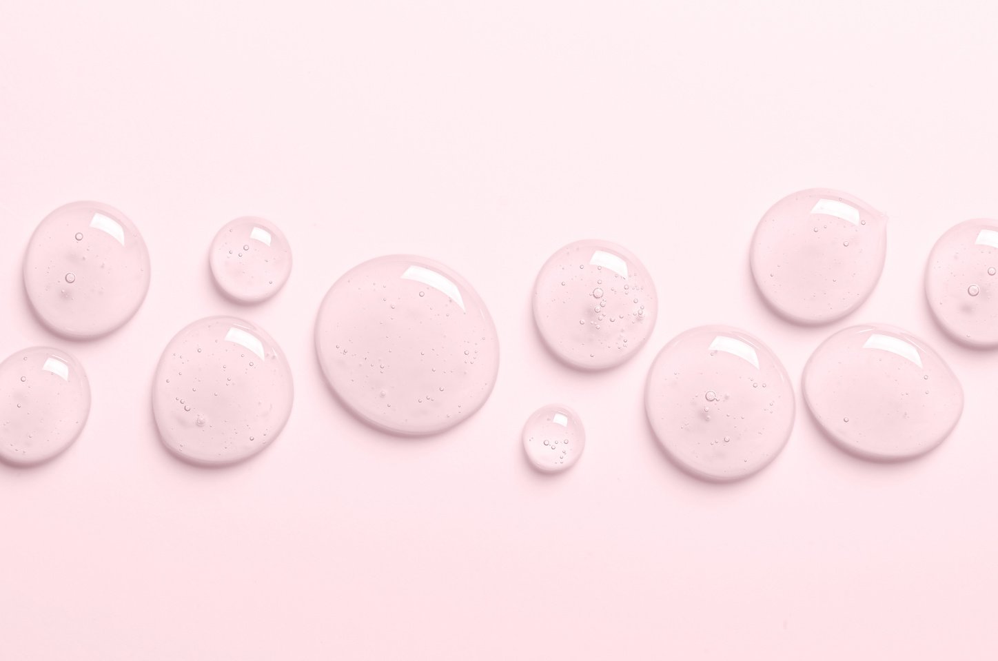 Pink drops of gel closeup. Cleansing facial scrub or shower gel or liquid soap drops. Copy space.