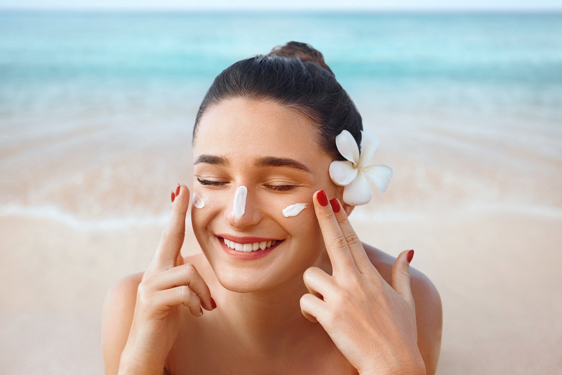 Beautiful woman applying cream sunscreen on a tanned face. Sunscreen. Skin and body care. The girl uses a sunscreen for her skin. Portrait of a female holding suntan lotion and moisturizing sunscreen.